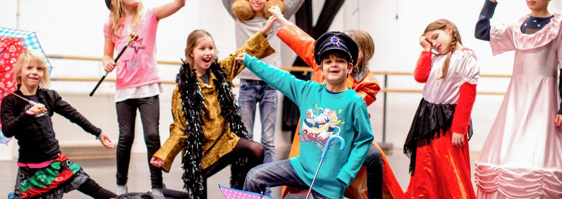 Een theatergroep van verschillende kinderen in kleurrijke verkleedkleren die op een speelse wijze poseren